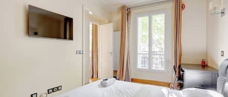 Una habitación de hotel con cama, televisión montada en la pared, ventana con cortinas y escritorio con silla.