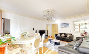 Ein Wohnzimmer mit Essbereich, einer Couch, einer Chandelierleuchtre und einem Kamin.
