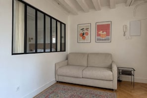 A living room with a sofa, a small side table, a patterned rug, and two framed pictures on the wall. - Cocon parisien • Rue de la Verrerie (Paris)