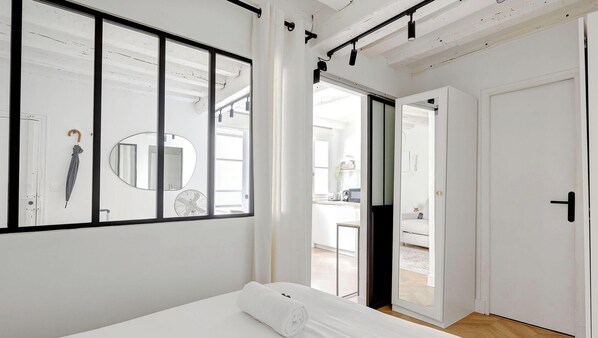 A bedroom with a large window, a mirror, a ceiling fan, and a door leading to a bathroom. - Elegance et confort a deux pas de Seine (Paris)
