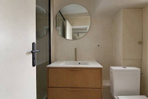A bathroom with a white sink, wooden cabinet, and a toilet. - Cocon parisien • Rue de la Verrerie (Paris)
