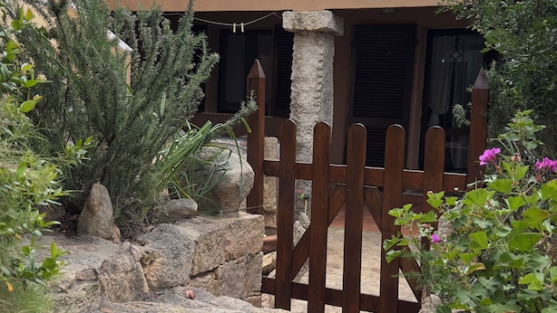 Un camino de piedra que lleva a una puerta de madera, rodeado de rocas y plantas.