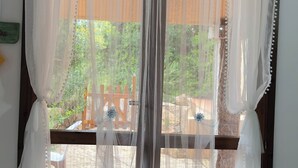 Una habitación con un gran ventanal cubierto por cortinas blancas translúcidas, piso de baldosas y una silla en primer plano.