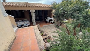 Un patio con suelo de baldosas, una mesa con sillas y una planta en maceta.