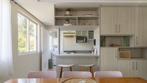 A modern kitchen with a built-in microwave, a small island with stools, and a dining table with chairs. - Beautiful apt 3 Minutes From Jurere Beach Vma101 (Florianópolis)