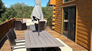A wooden deck with a table and chairs, a covered umbrella, and a view of the surrounding forest. - Modern 3BR/4BA Windham chalet w/ hot tub, views & mins to ski, bars, dining! (Windham)