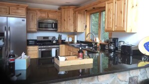 A modern kitchen with wooden cabinets, a stainless steel refrigerator, a microwave, a stove, and a large island with a sink. - Modern 3BR/4BA Windham chalet w/ hot tub, views & mins to ski, bars, dining! (Windham)
