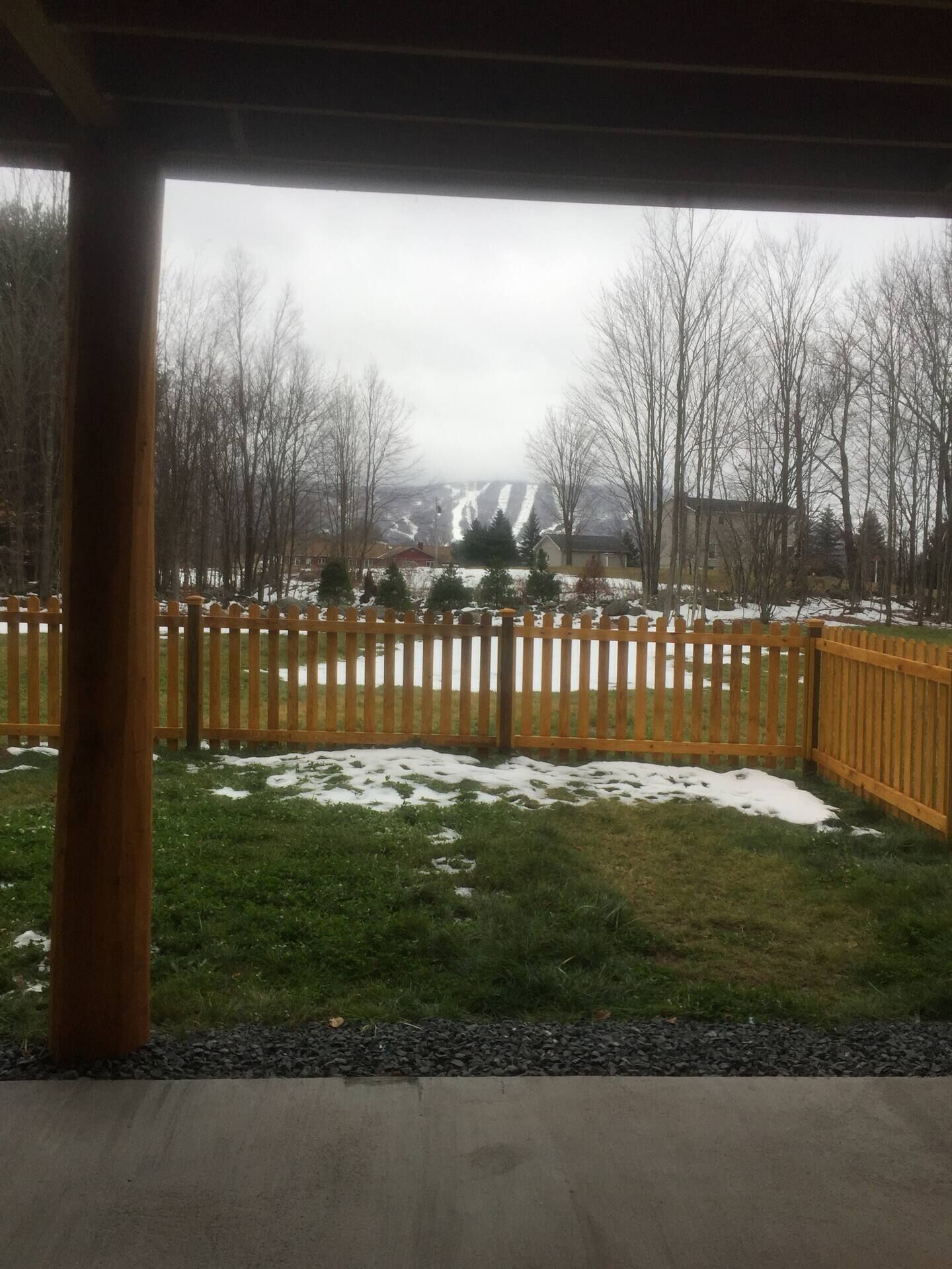 A covered outdoor area with a wooden fence, snow on the ground, and leafless trees in the background.