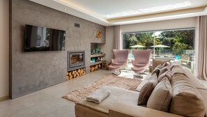 Ein modernes Wohnzimmer mit Flachbildfernseher, Kamin, einer Couch und Blick auf einen Außenpool.