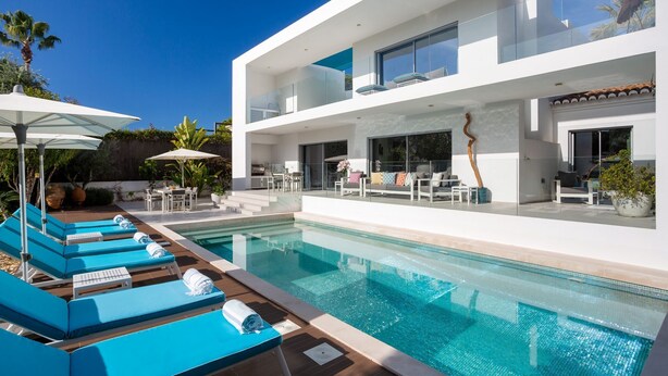 Ein modernes, zweistöckiges Haus mit Swimmingpool, Sitzgelegenheit im Freien und Blick zum Himmel.