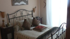 A bedroom with a bed, a nightstand, a wall-mounted lamp, and a window with curtains.