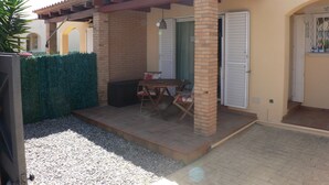 A covered patio with a table and chairs, a brick pillar, and a door with shutters.