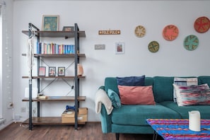 A living room with a teal sofa, a wooden ladder bookshelf, and decorative plates on the wall. - Stylish 1BD with Sunny Terrace, Honor Oak Park (Greater London)