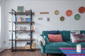 A living room with a teal sofa, a wooden ladder bookshelf, and decorative plates on the wall.