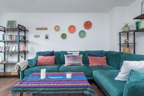 Un salon chaleureux avec un canapé de couleur turquoise, des coussins colorés, un tapis à motifs et une bibliothèque remplie de livres.