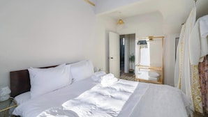 A hotel room with a large bed, a bedside table, a mirror, and a door leading to another room.