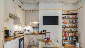 A modern kitchen with a dining area, a bookshelf, and a flat-screen TV.
