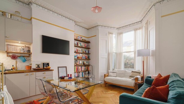 A spacious living area with a sofa, a coffee table, a bookshelf, and a large window.