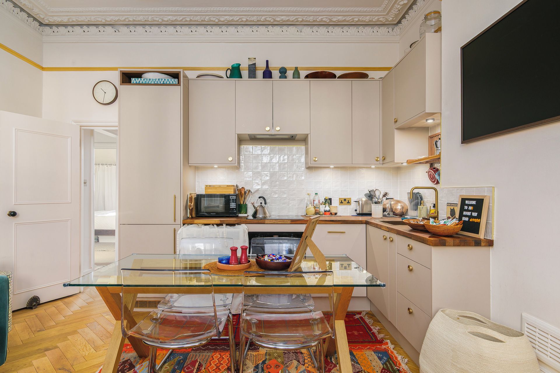 A modern kitchen with a glass dining table, white cabinetry, and a clock on the wall.