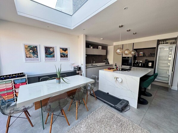 A modern kitchen with a central island, a dining area with clear chairs, and a small exercise area.