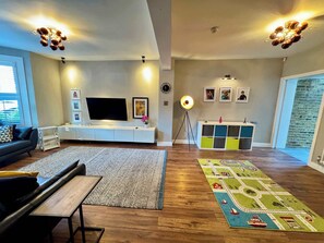 A modern living room with a flat-screen TV, a white entertainment unit, a colorful rug, and a wooden floor.