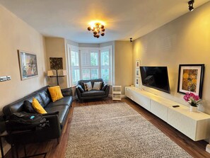 A living room with a black leather sofa, a white entertainment unit, and a large flat-screen TV.