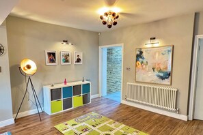 A room with a radiator, a colorful play area, a chandelier, and framed pictures on the wall.