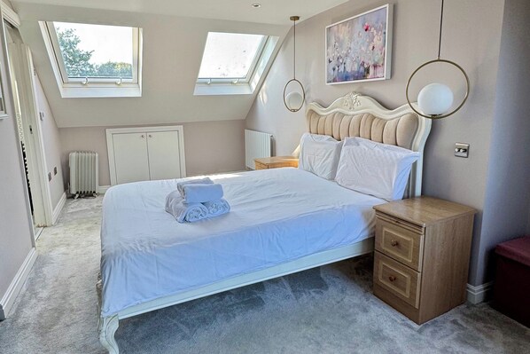 A bedroom with a large bed, two bedside tables, a radiator, and a skylight.