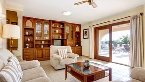 A spacious living room with a sofa, armchairs, a wooden cabinet, and a ceiling fan. - Villa Los Leones - Three Bedroom Villa, Sleeps 6 (Alayor)