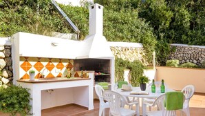 An outdoor kitchen with a stone wall and a tiled backsplash, surrounded by white chairs and a table. - Villa Los Leones - Three Bedroom Villa, Sleeps 6 (Alayor)