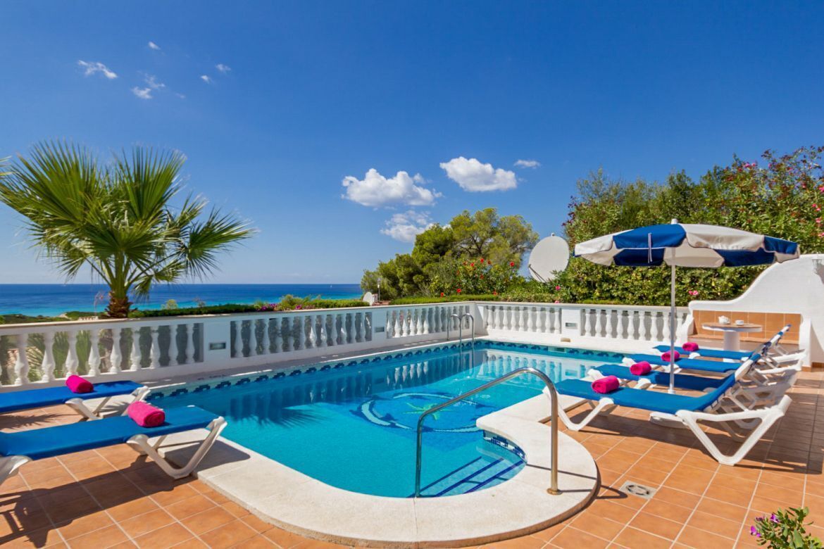 A pool area with lounge chairs and a view of the sea.