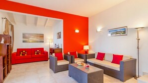 A modern living room with a red accent wall, wicker furniture, and a view of the cityscape.