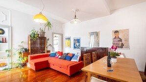 A living room with a red sofa, wooden dining table, and various plants.