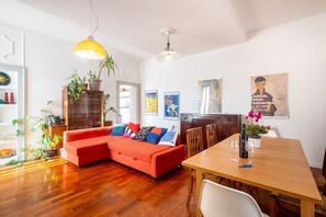 A living room with a red sofa, wooden dining table, and various plants.
