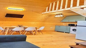 Et hyggeligt sommerhusinteriør med spiseplads, sofa, køkken og et åbent loftsrum.