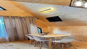 Et træpanelt interiør med et spisebord og stole, et skråt loft med en lampe, og et vindue med gardiner.