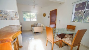 A dining area with a round table, four chairs, a sofa, and a wooden counter. - Casa Pet-friendly com Wi-fi e Churrasqueira (Itanhaém)