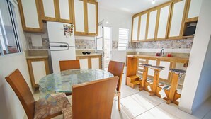 A compact kitchen with wooden cabinets, a glass dining table, and a small bar area. - Casa Pet-friendly com Wi-fi e Churrasqueira (Itanhaém)