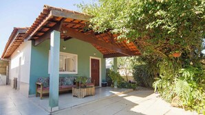 A house with a tiled patio, a wooden pergola, a sofa, and a table with plants. - Casa Pet-friendly com Wi-fi e Churrasqueira (Itanhaém)
