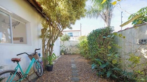 A narrow pathway with a bicycle parked on the left, surrounded by greenery and a building with a window. - Casa Pet-friendly com Wi-fi e Churrasqueira (Itanhaém)