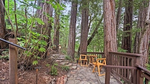 A wooden staircase leading up to a wooden deck with benches and tables, surrounded by tall trees.
