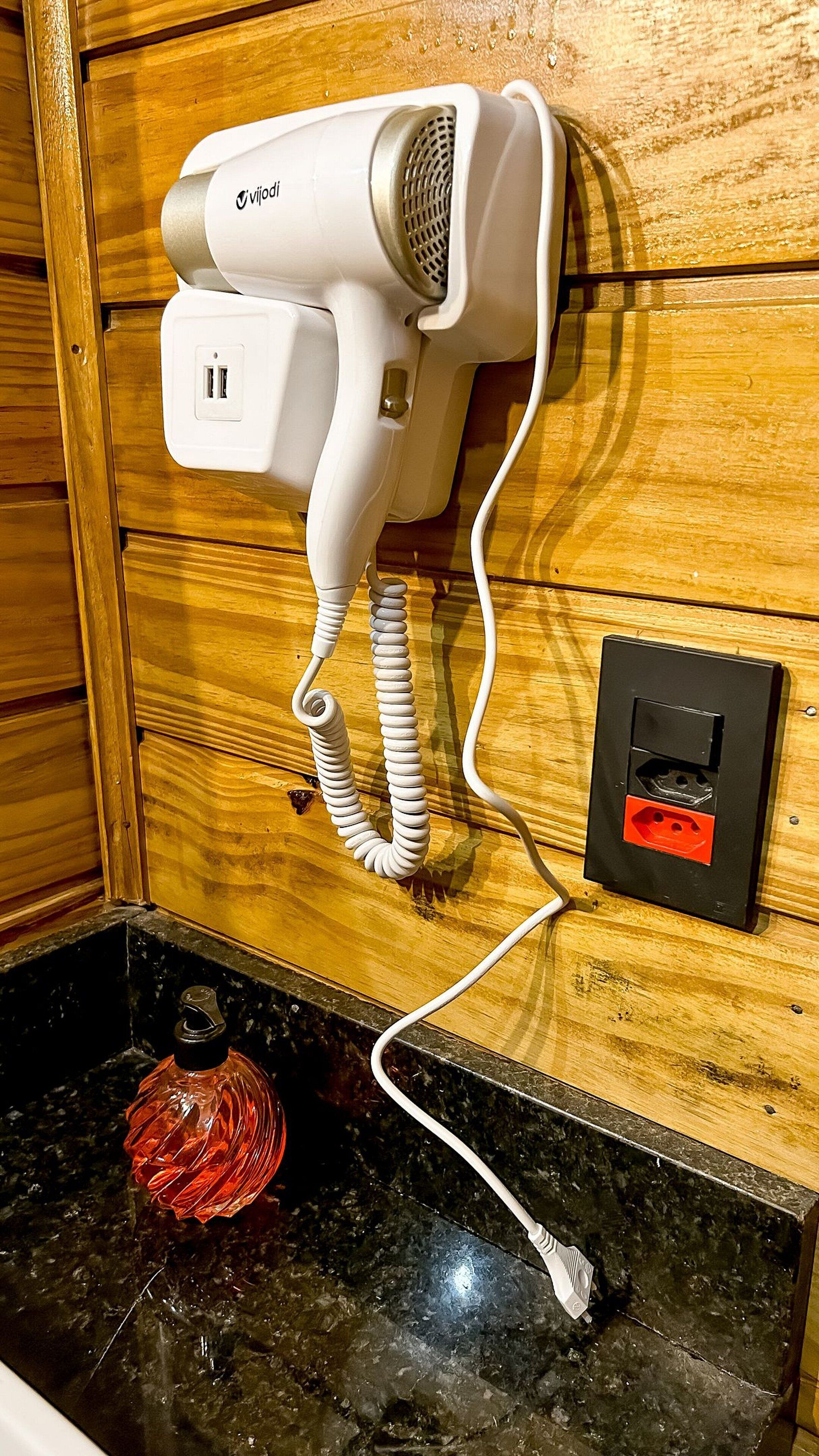 A hair dryer mounted on a wooden wall, connected to a power outlet.