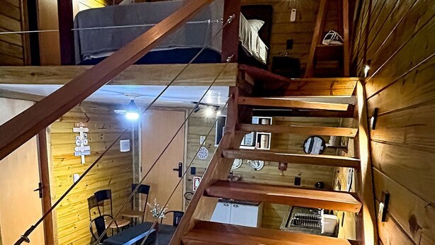 A wooden staircase with a view of a dining area and kitchen on the upper level. - Casa de Praia (Buzios)