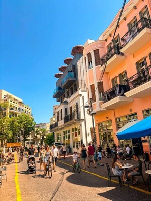 A street with buildings, outdoor seating, and people walking.