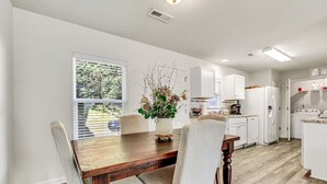 A modern kitchen with white cabinets, a wooden dining table, and a vase with flowers.