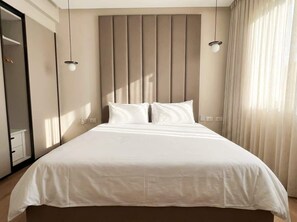Una cama grande con cabecera, dos lámparas de noche y una ventana con cortinas.