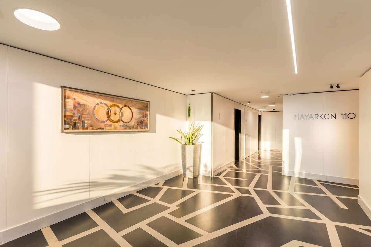 Ein moderner Hotelkorridor mit geometrischem Bodenmuster, einem großen abstrakten Gemälde und einem Topf mit Pflanze.