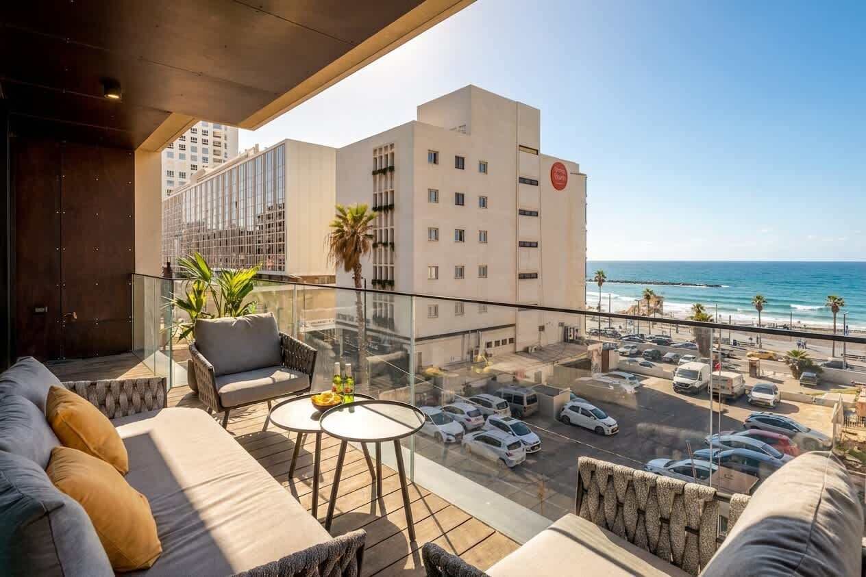 En balkon med udsigt over havet, en parkeringsplads og en bygning med et rødt logo.