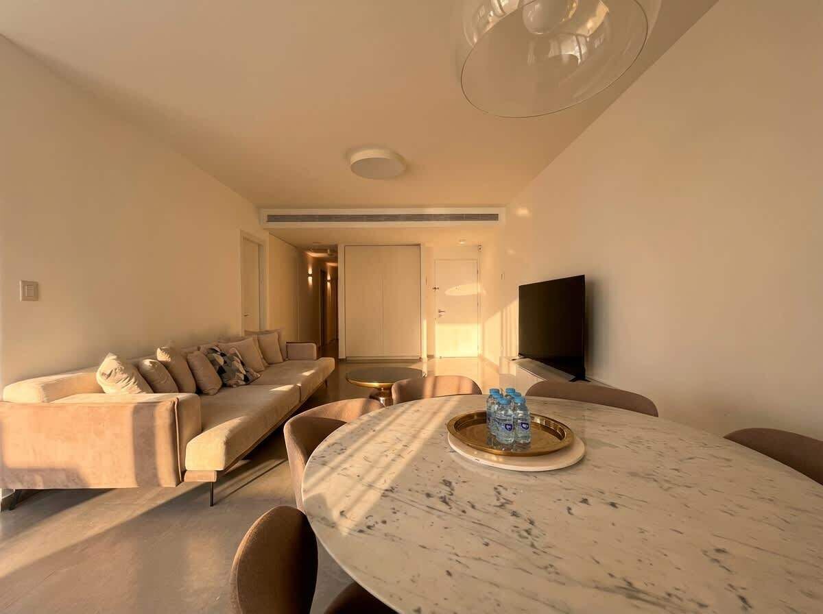 A modern living room with a marble table, beige sofas, and a flat-screen TV.