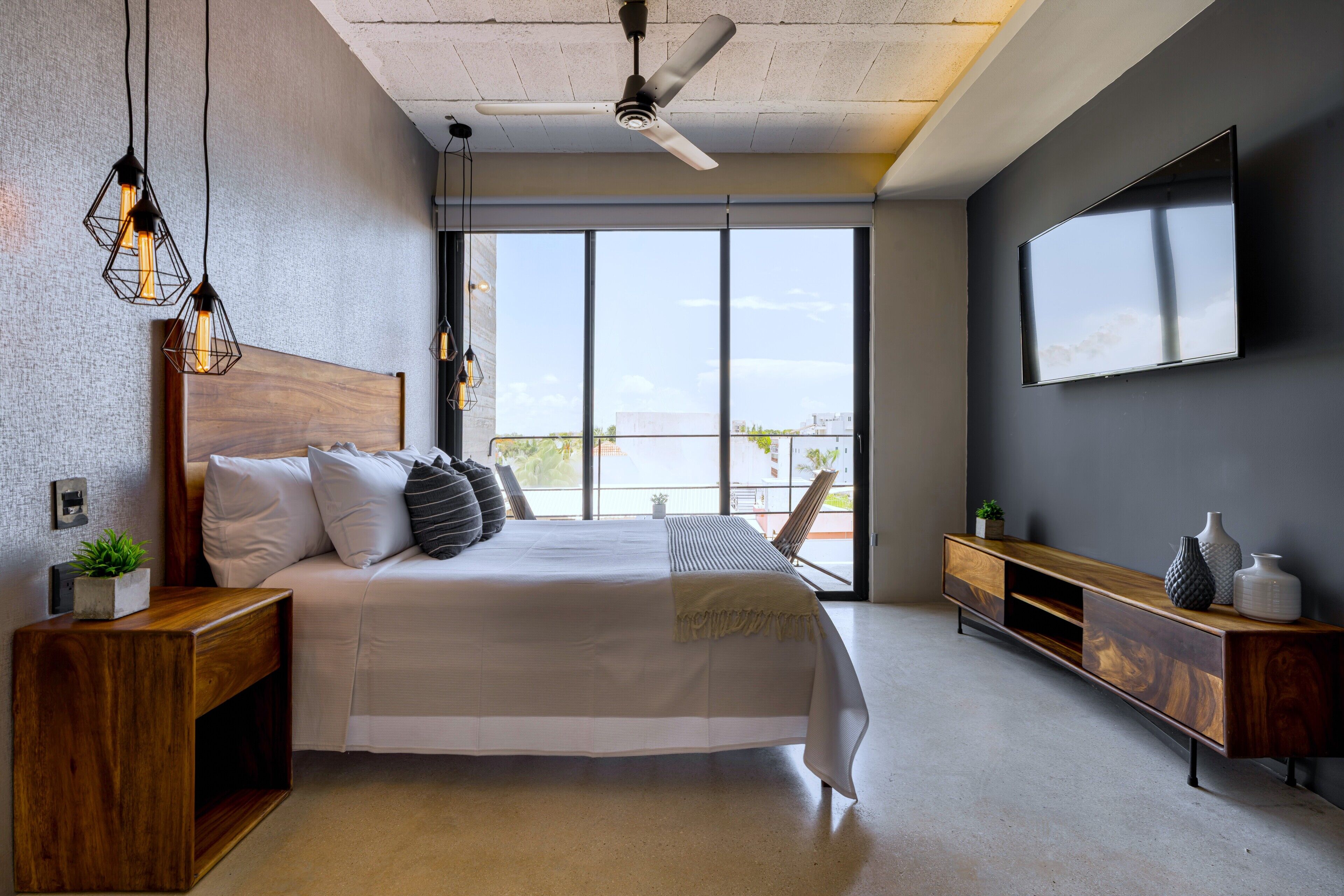 A modern bedroom with a large bed, a wooden nightstand, a console table, and a TV mounted on the wall.